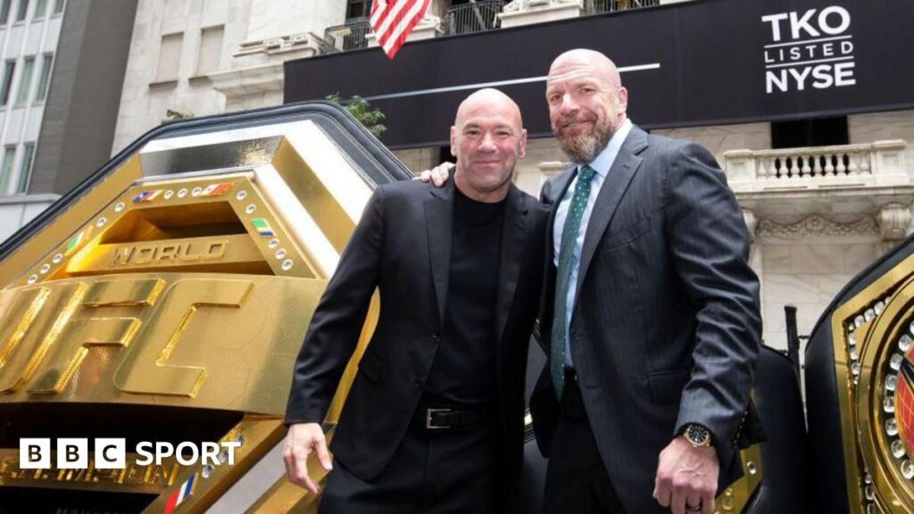 Dana White and Paul Levesque stand beside each other beside a massive UFC belt